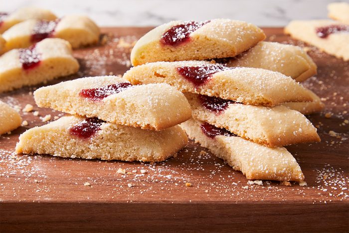 Close-up shot of a pile of Split-Second Cookies on a wooden board, showing jam centers and sugar dusting.