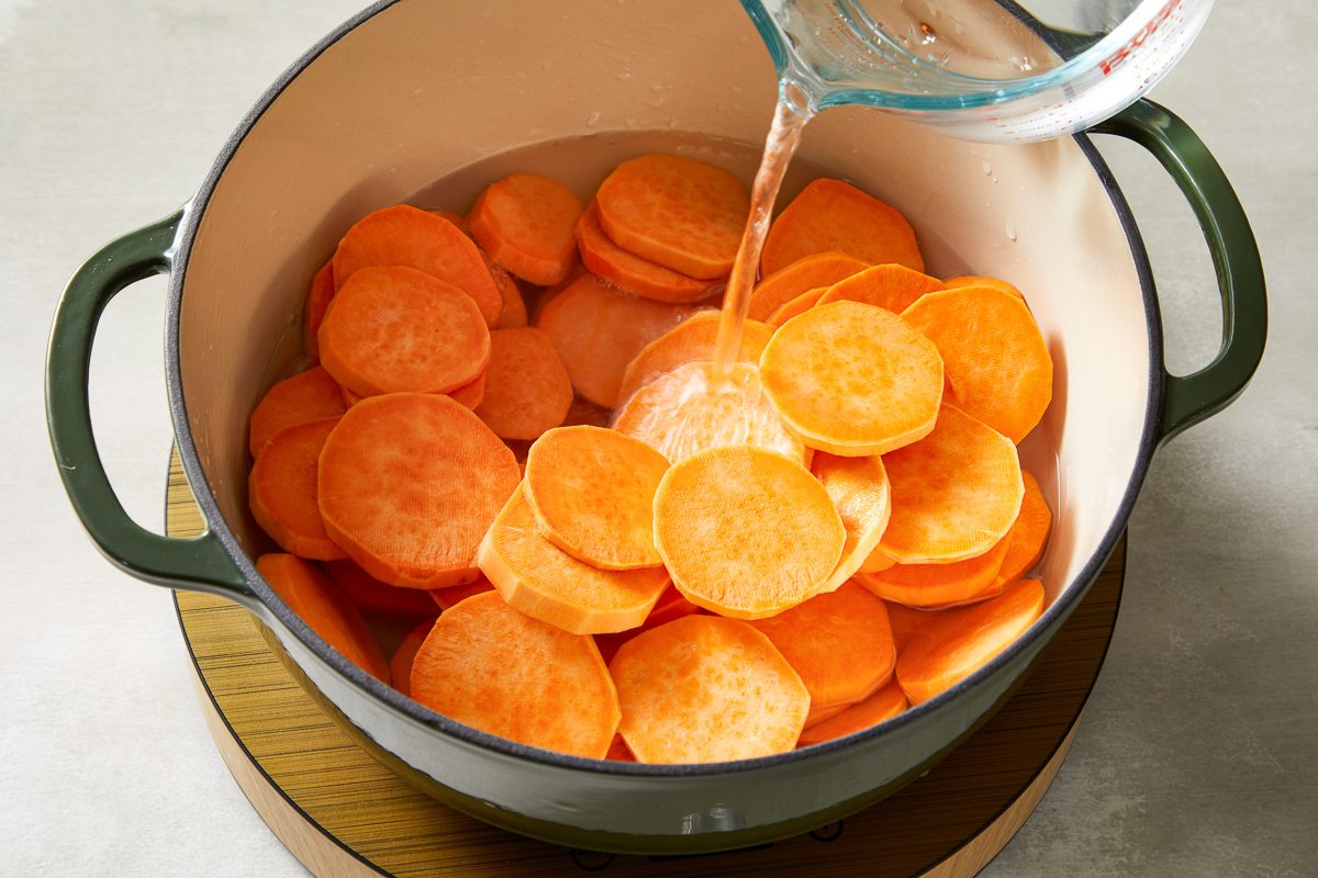 water being poured onto peeled sweet potatoes in a dutch oven