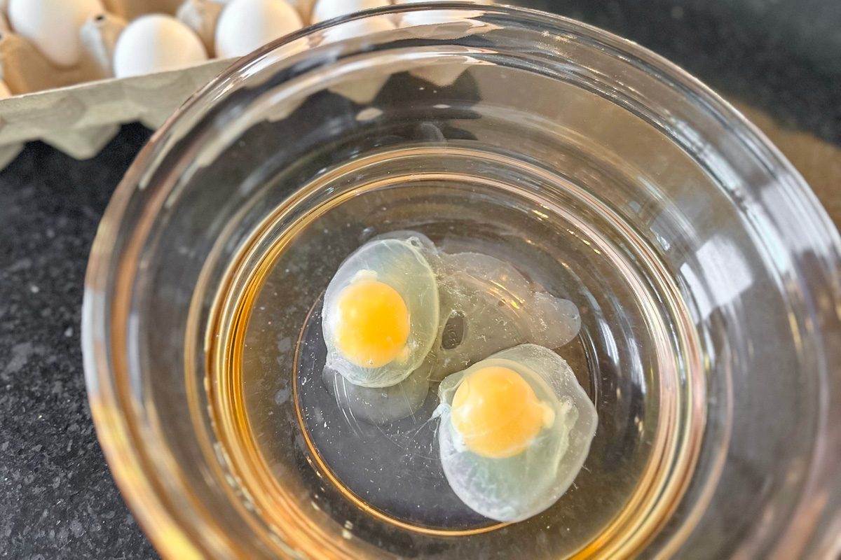 eggs cracked into water and vinegar mixture in a bowl