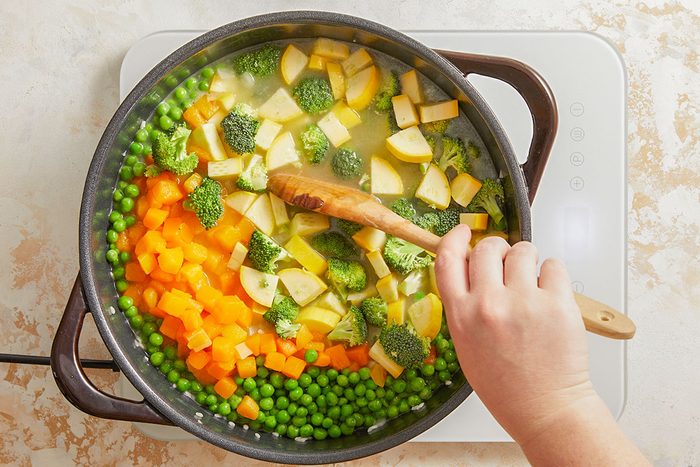 Overhead shot of a colorful mixture of peas, carrots, and zucchini added to the pot of risotto.