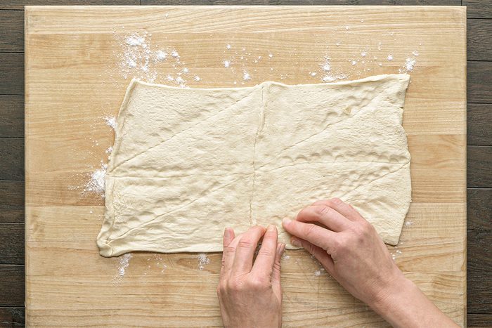 This is a close-up shot; two hands fold dough on a wooden surface dusted with flour