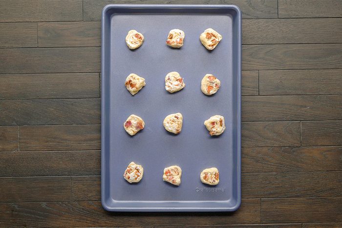 Overhead shot; a baking sheet holds 12 dough balls with meat and cheese bits on a dark wood surface