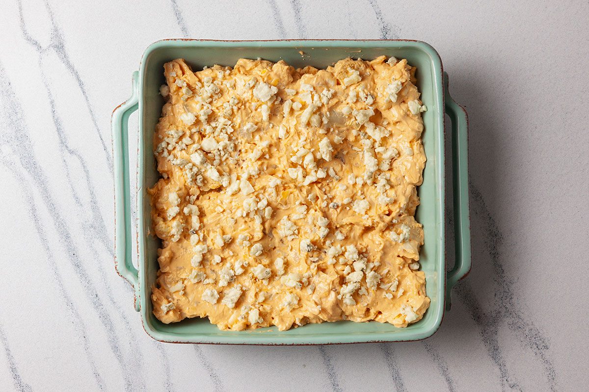 Overhead shot of a baking dish filled with creamy cauliflower mixture, evenly spread and ready for baking, set on a light marble surface;