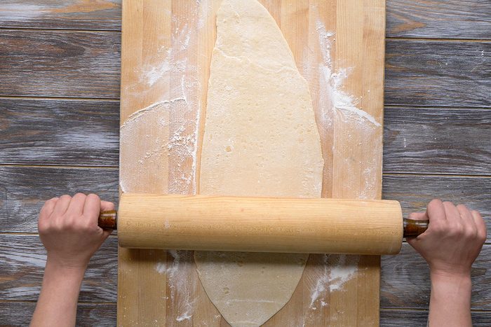 Overhead shot of a hands roll out dough with a pin on a floured wooden surface and cutting board the scene shows baking preparations in progress