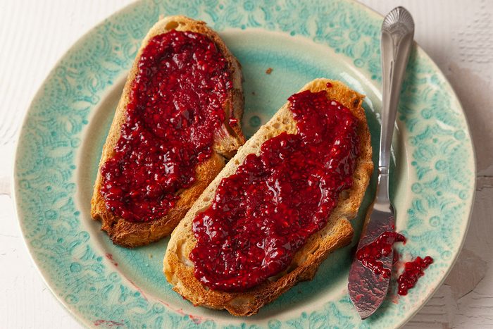 Overhead shot of toast slices generously spread with glossy red chia seed jam on a patterned plate, with a butter knife alongside;