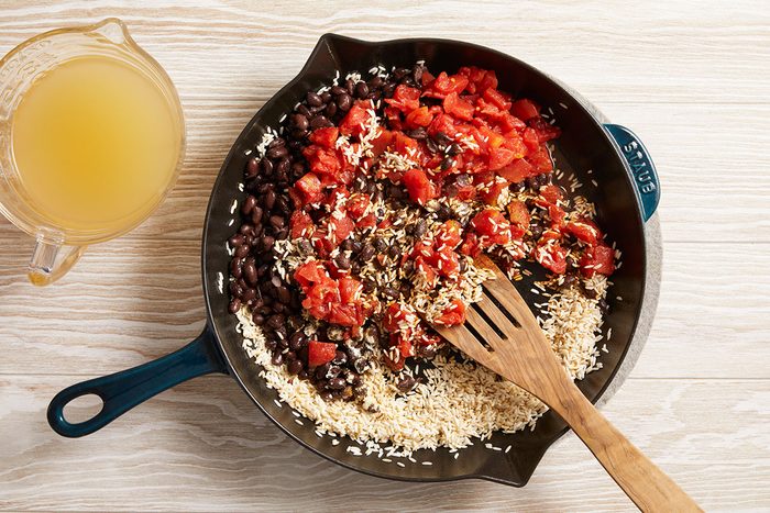 Overhead shot of black beans, diced tomatoes, and rice being mixed with broth.