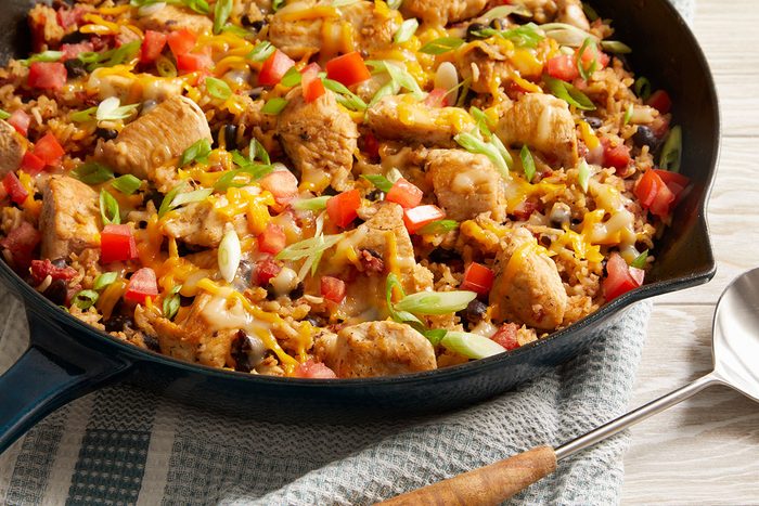 Close up shot of the skillet showcasing Chicken Burrito Skillet over a blue-and-white striped cloth, and a spoon