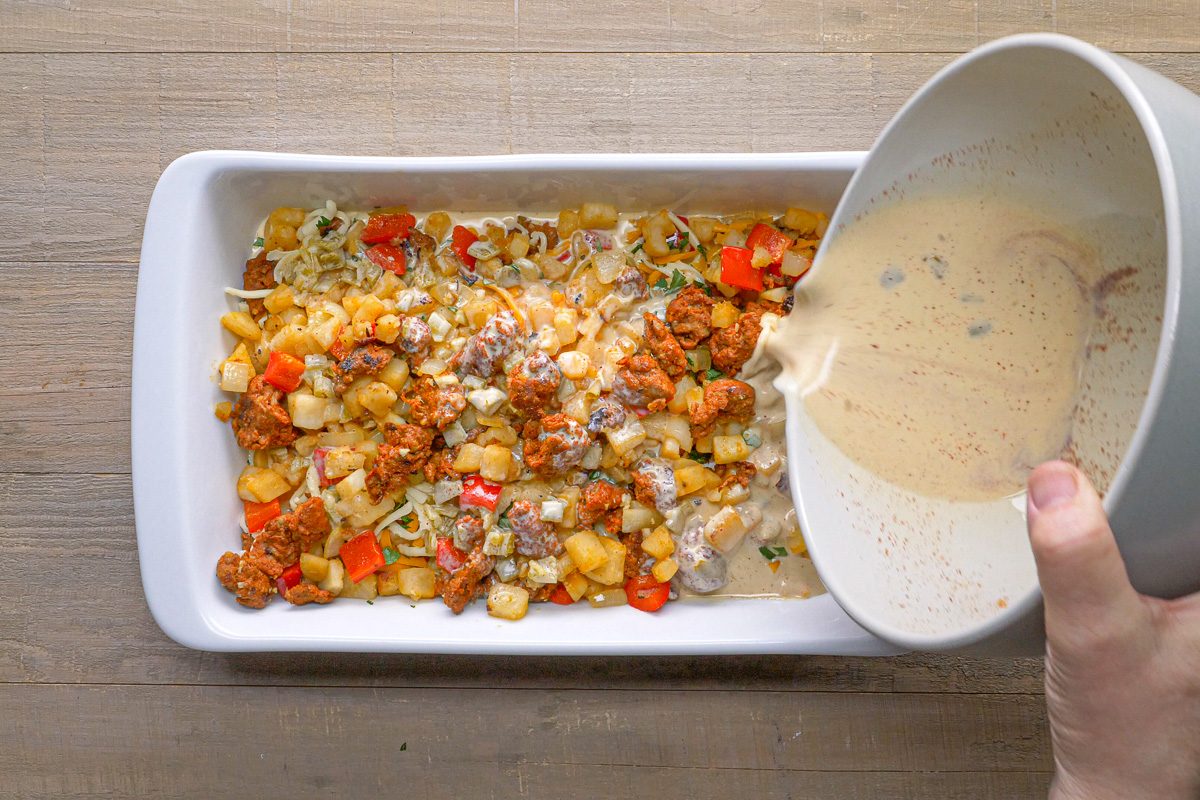 casserole layers being topped with cheese and eggs mixture