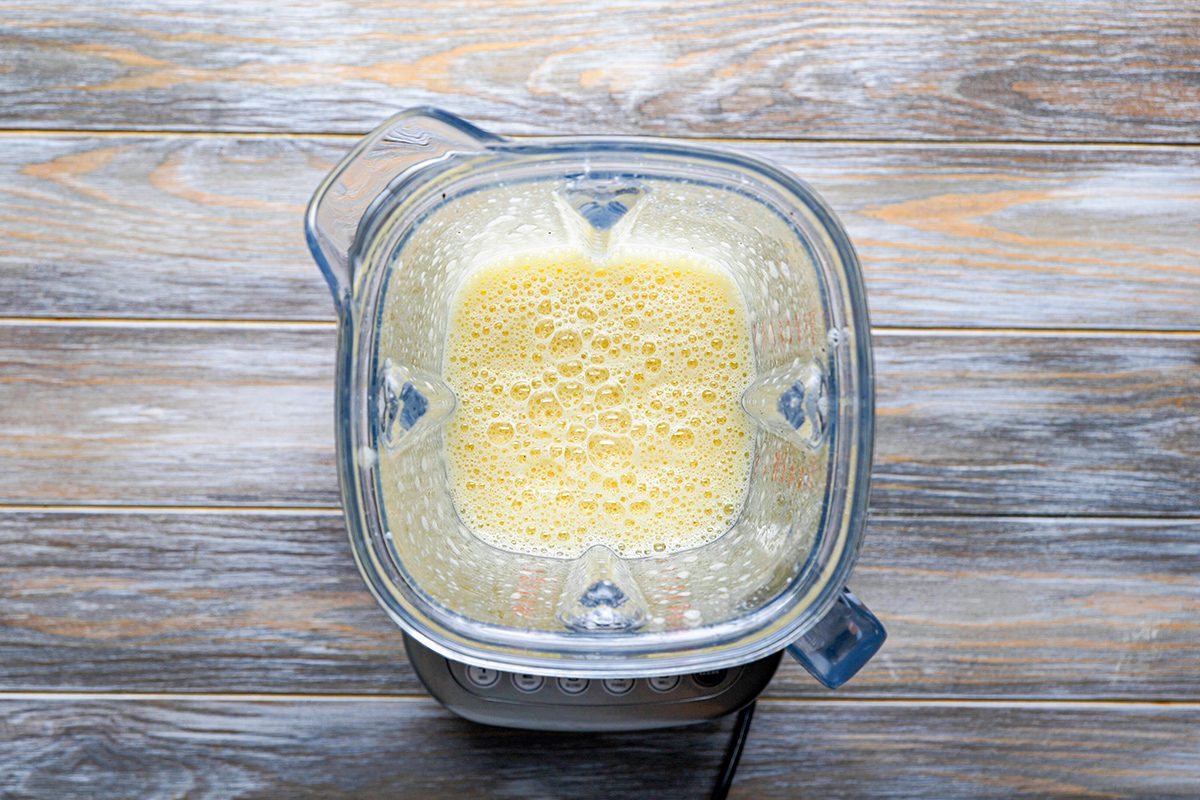A top-down view of a blender filled with a frothy light yellow liquid, sitting on a wooden surface.