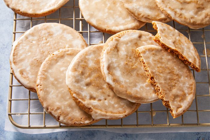 3/4th shot of Gingerbread Latte Cookies sit on a cooling rack one is broken to display its spiced soft inside all are covered with glaze