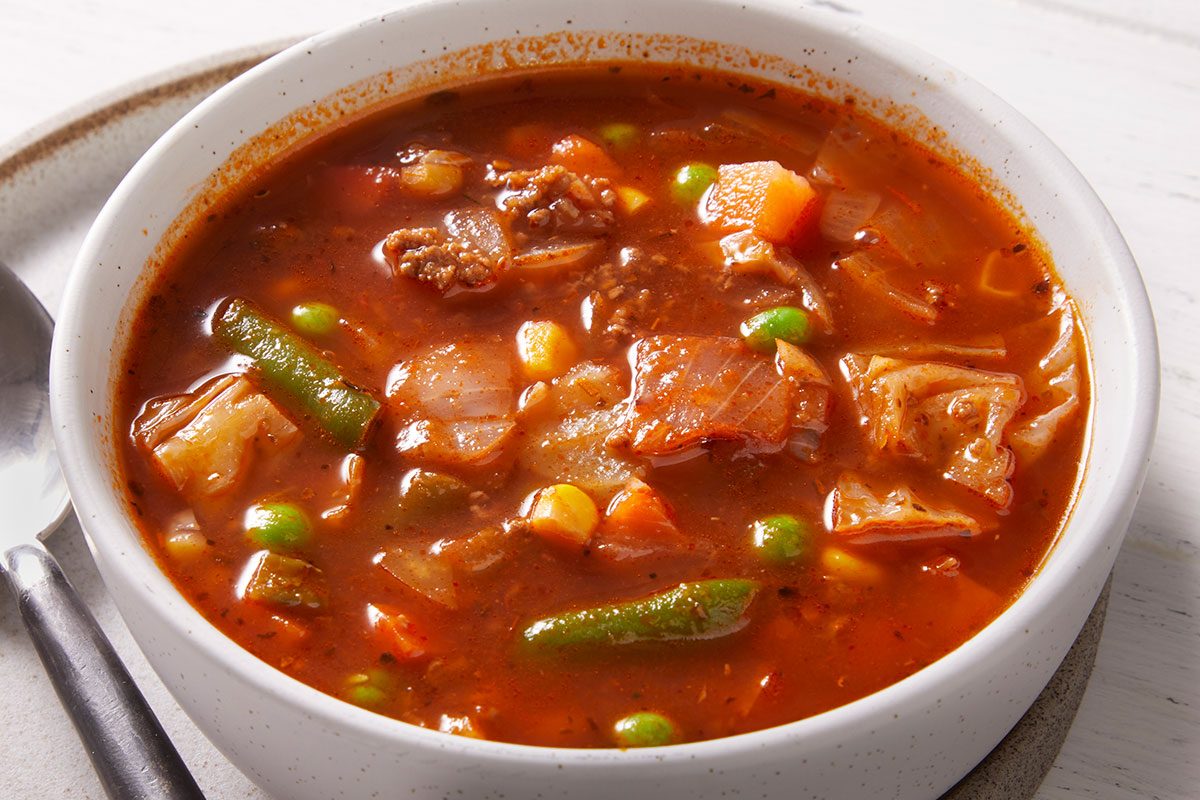 Close-up overhead shot of a white bowl filled with Italian Veggie Beef Soup showing beef pieces, green beans, and mixed vegetables in a tomato base.