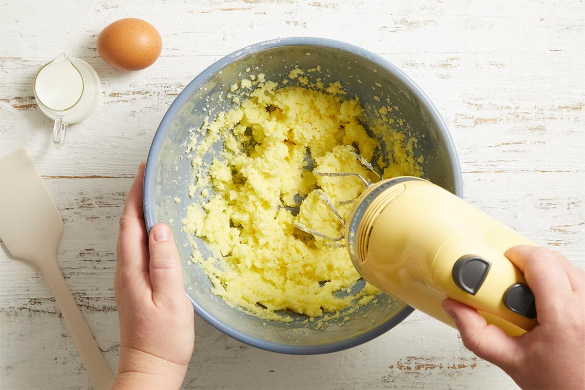 Overhead shot of cookie dough being mixed in a bowl with a hand mixer, butter and sugar visibly creamed together.