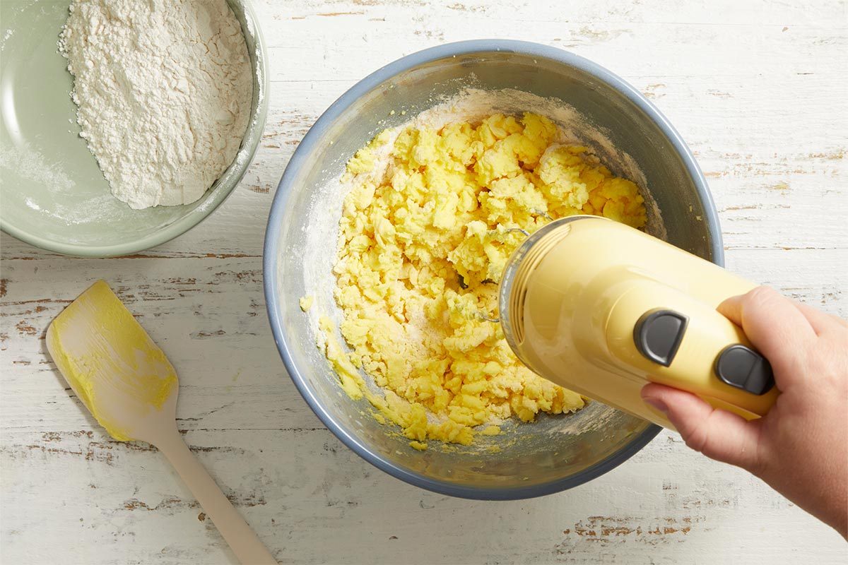Close-up overhead view of dough mixture being further whipped in a mixing bowl with a hand mixer.