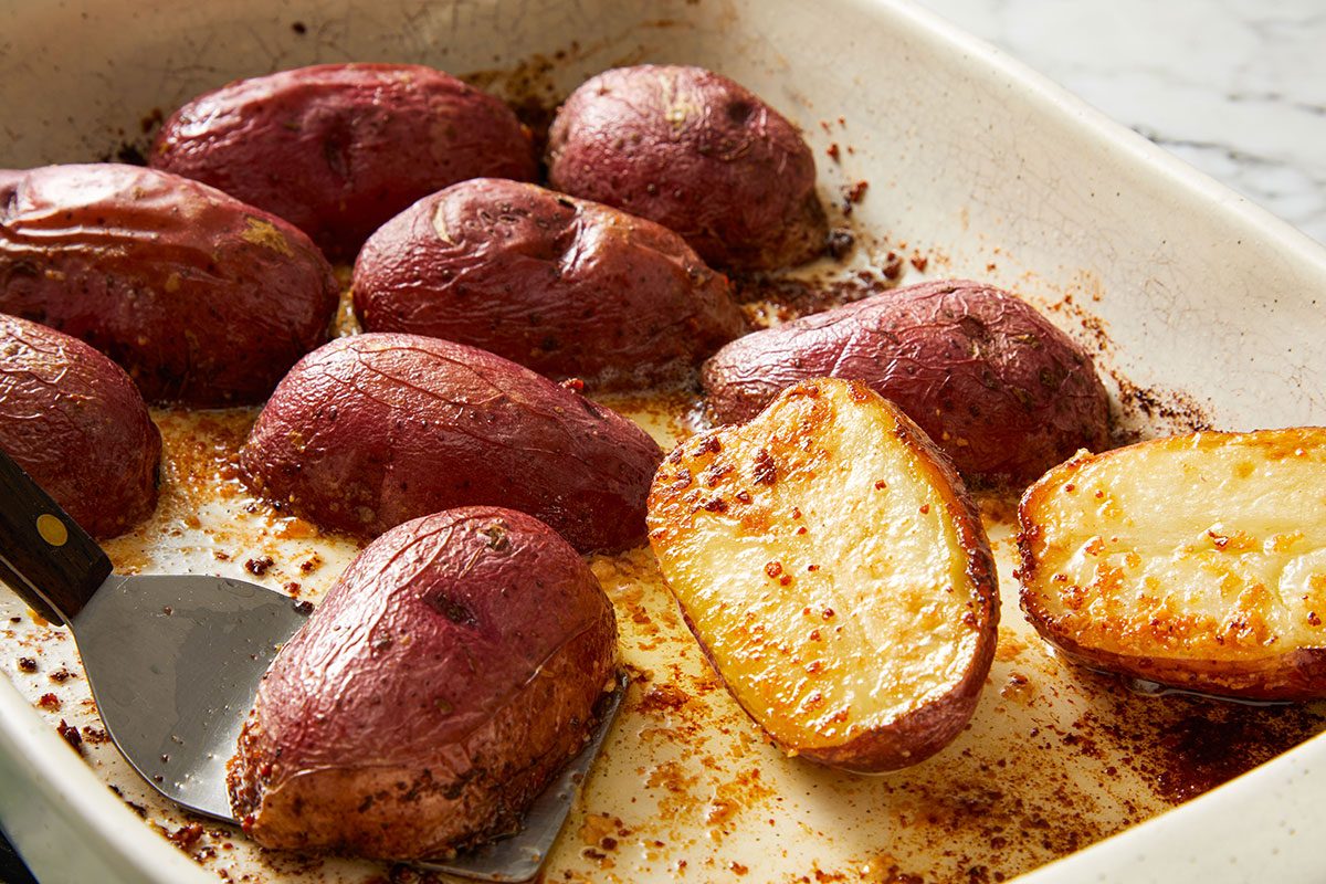 Close up shot of a white baking dish filled with halved Parmesan Baked Potatoes and seasonings, just out of the oven.