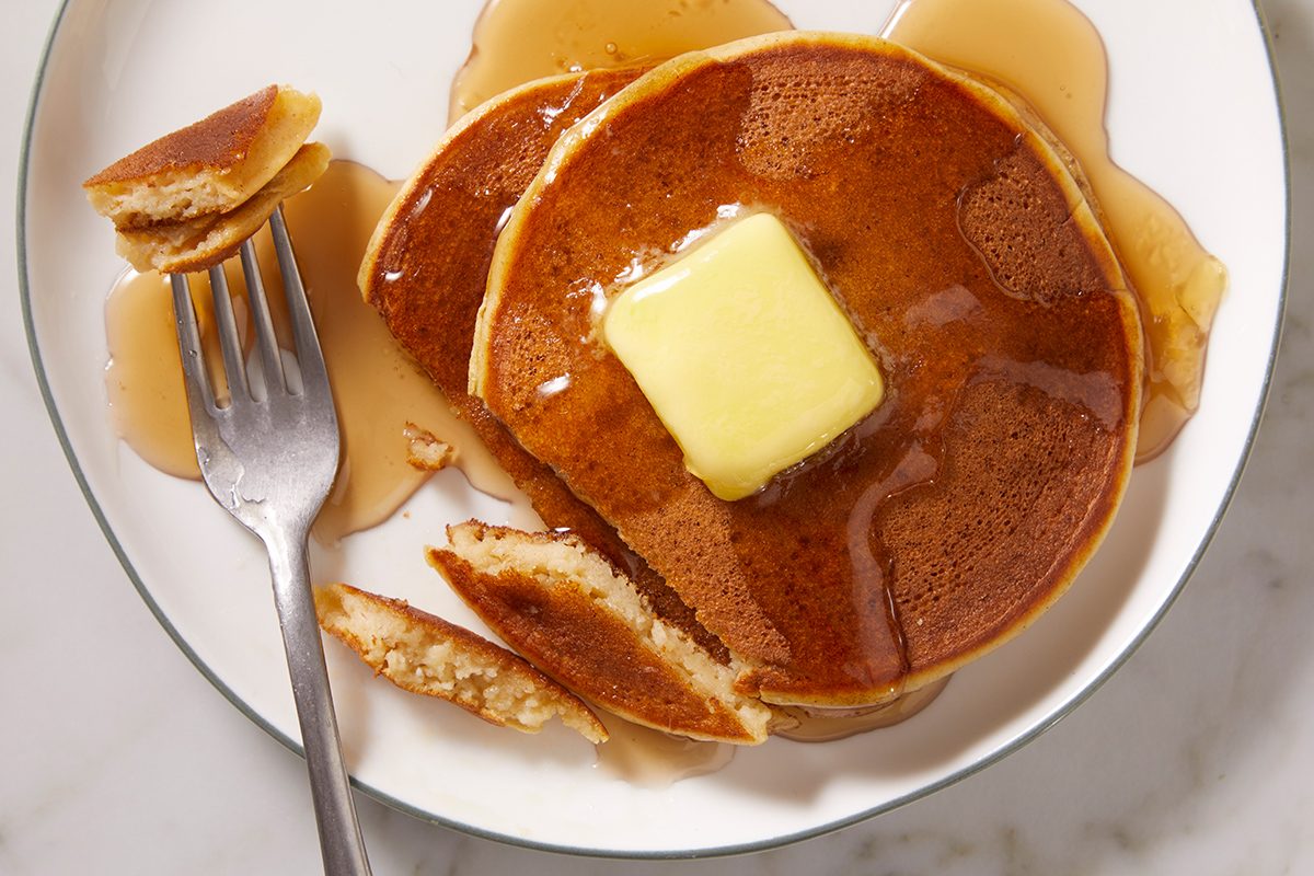 A plate of pancakes topped with a pat of butter and syrup, with a fork holding a piece of pancake on the side.