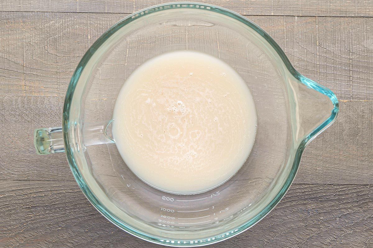 Overhead shot of a glass measuring cup containing a small amount of milky liquid, placed on a wooden surface;