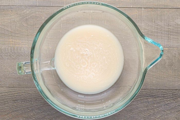 Overhead shot of a glass measuring cup containing a small amount of milky liquid, placed on a wooden surface;