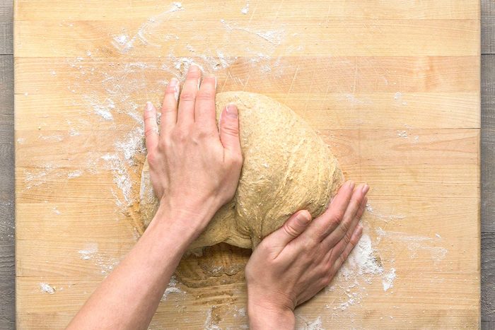 Overhead shot of two hands kneading a ball of dough on a floured wooden cutting board;