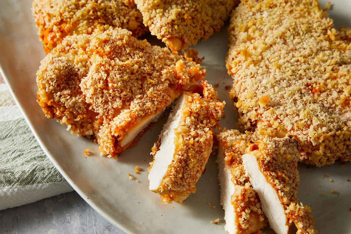 A plate with several pieces of golden, crispy baked chicken breast, some sliced to show the white, juicy interior. The chicken is coated in a crunchy breading.