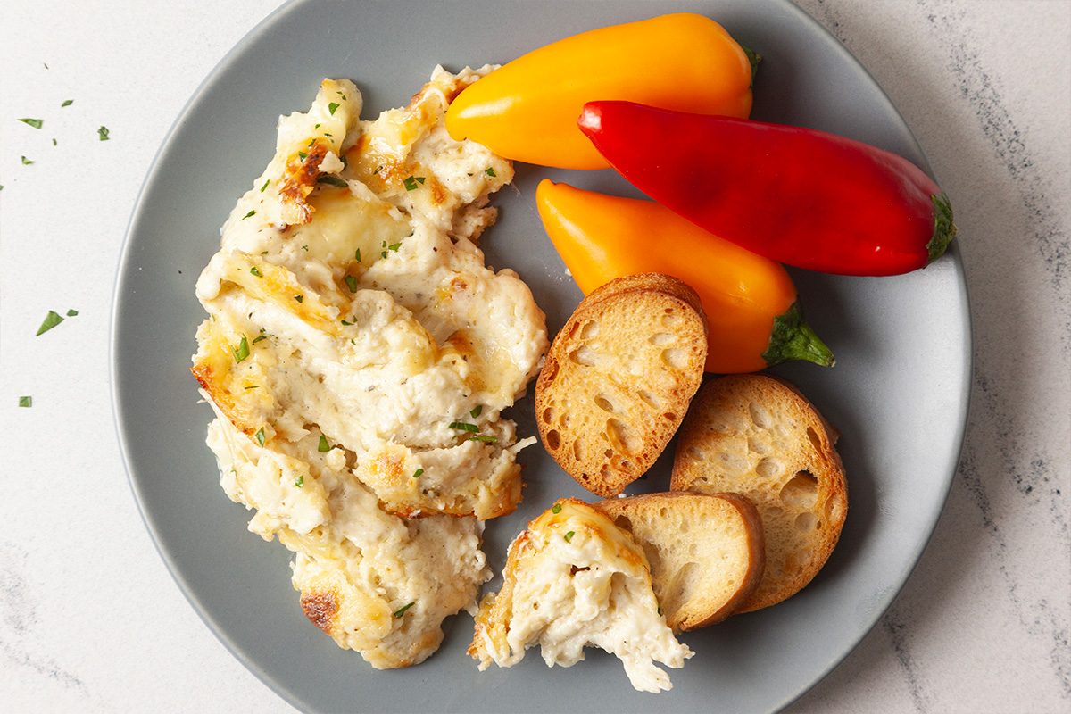 A plated serving of Cheesy Chicken Alfredo Dip accompanied by crostinis, crackers, and fresh vegetables. The creamy dip features shredded chicken, melted mozzarella, Parmesan cheese, and herbs, presented as a ready-to-serve appetizer for entertaining.