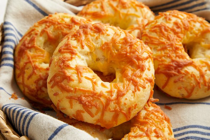 Closeup shot of golden cottage cheese bagels topped with melted shredded cheese in a basket lined with a blue-striped cloth;