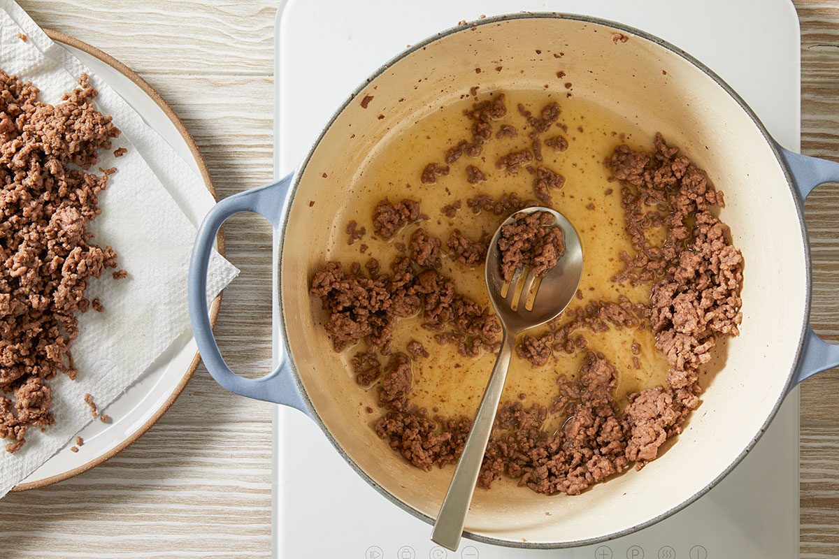 Overhead step-by-step trend food photography showing ground beef browning in a Dutch oven with olive oil at the beginning of a Dirty Cabbage recipe.