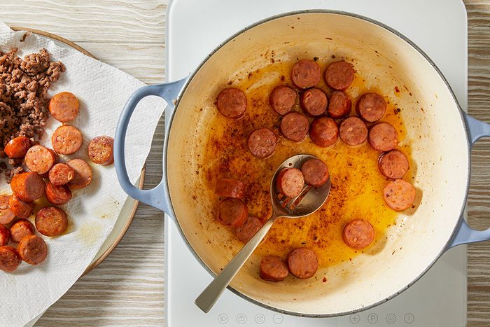 Overhead step-by-step trend food photography of sliced andouille sausage sautéing in a Dutch oven for a Dirty Cabbage recipe.