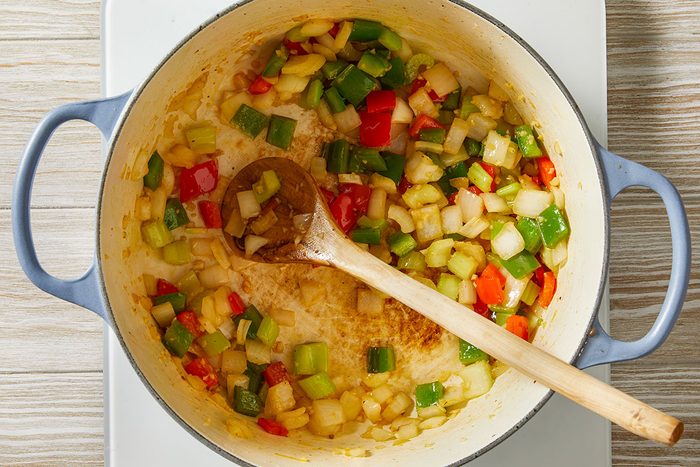 Overhead step-by-step trend food photography showing chopped onion, celery, and red and green peppers being cooked in a Dutch oven for Dirty Cabbage.