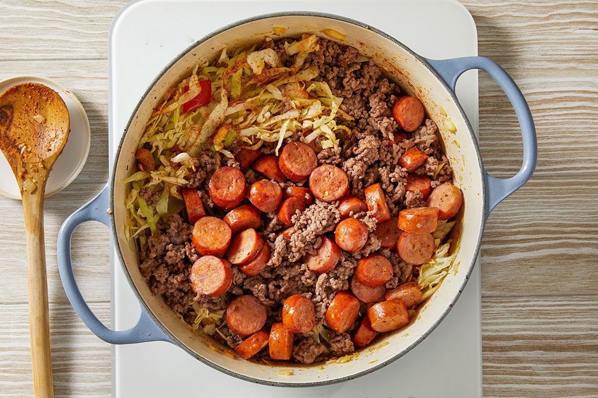 Overhead step-by-step trend food photography showing ground beef and andouille sausage mixed with shredded cabbage in a Dutch oven.