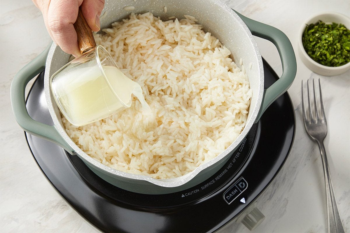 Cooked jasmine rice in a pot as butter is added for richness before finishing with lime juice and fresh cilantro. This step highlights the preparation of cilantro lime rice for a fish taco bowl.