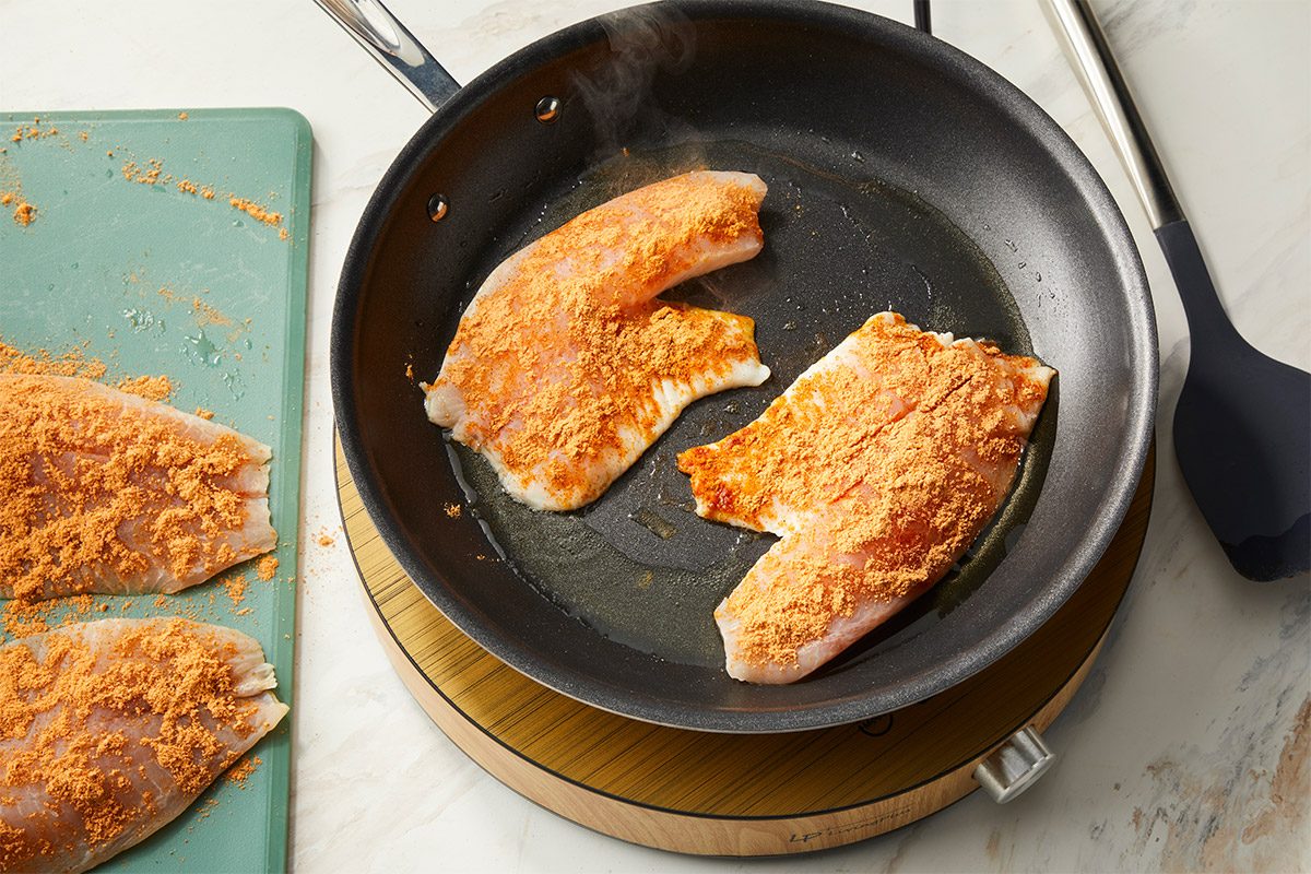 Tilapia fillets coated in taco seasoning sear in a nonstick skillet with olive oil until golden and flaky. This step captures the protein preparation for a fish taco bowl.
