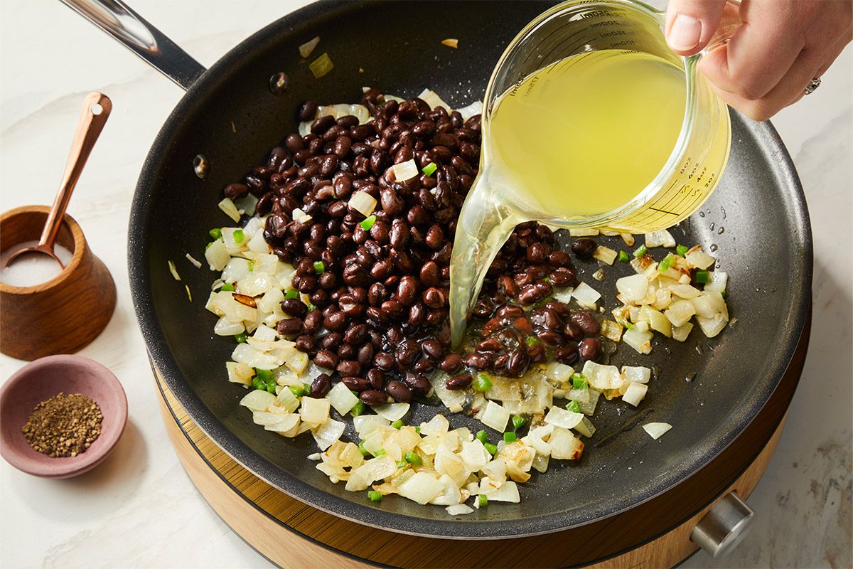 Black beans and reduced-sodium chicken broth are poured into the skillet with sautéed onions and peppers, creating a flavorful component for the fish taco bowl.