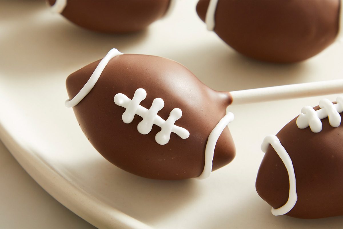 Overhead extreme close-up of a single football cake pop showing smooth chocolate coating and detailed white icing laces.