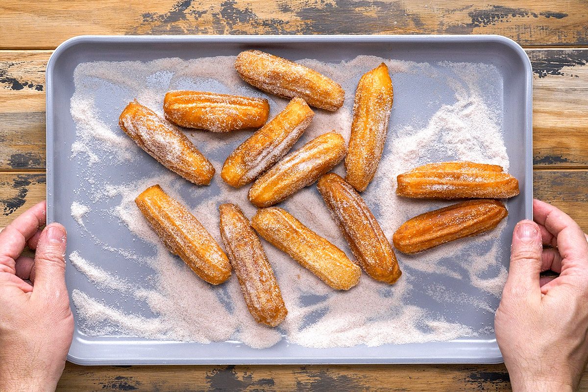 Overhead shot of Homemade churros resting on sugar each one dusted generously the tray sits on a rustic wooden surface