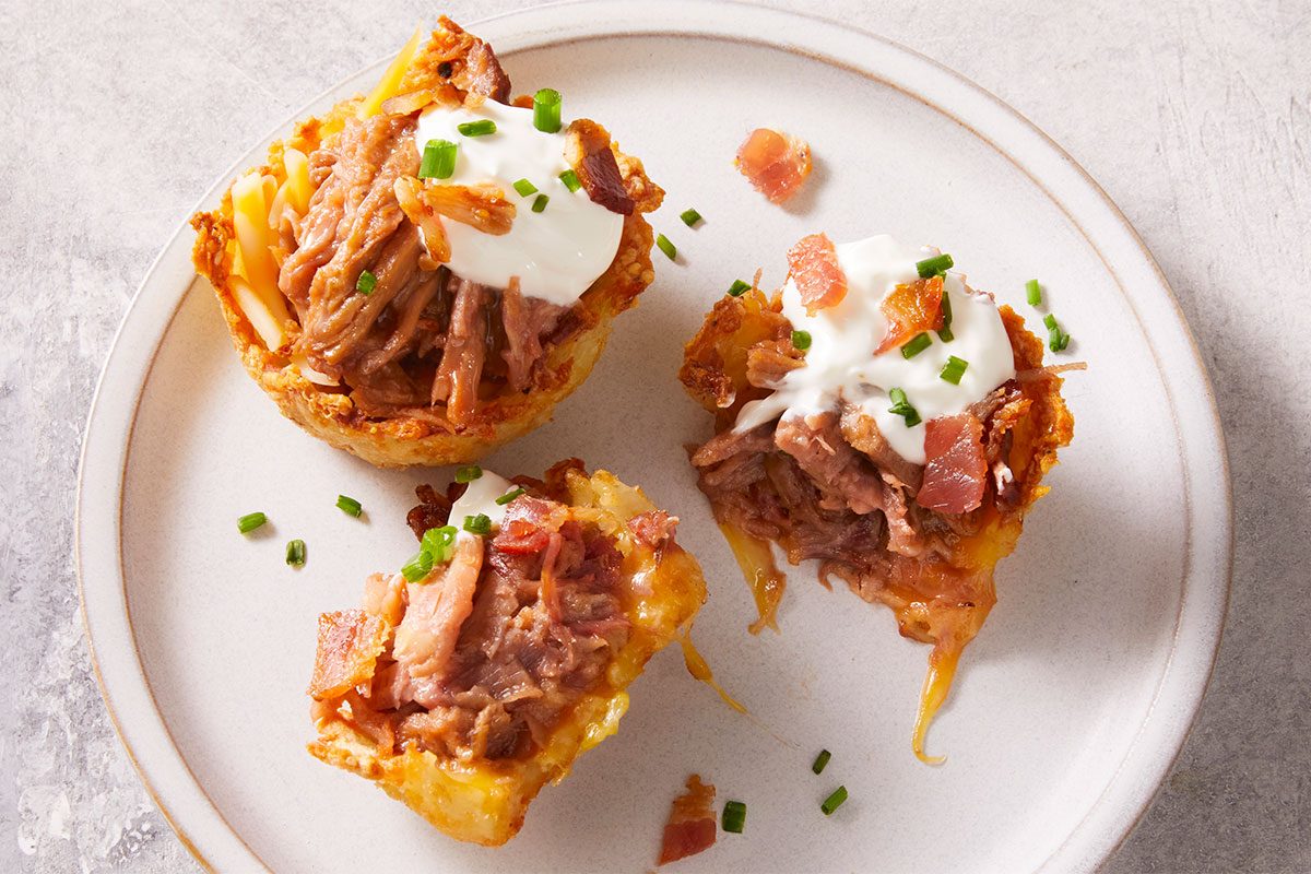 Close up shot of Loaded pulled pork muffin cups with cheese, bacon, and chives, served on a white plate