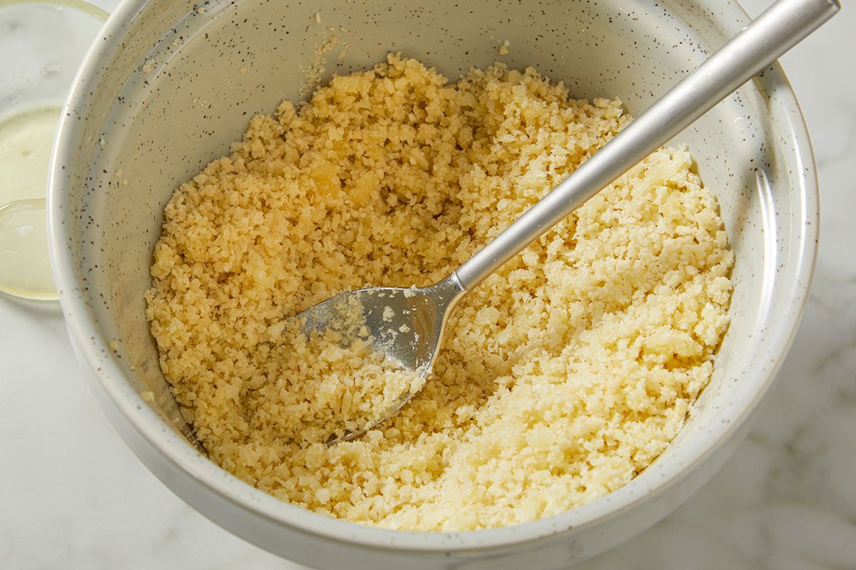 An overhead, horizontal step-by-step image showing panko breadcrumbs mixed with grated Parmesan cheese and melted butter in a bowl. This mixture is prepared as a crispy topping for Million-Dollar Gnocchi.