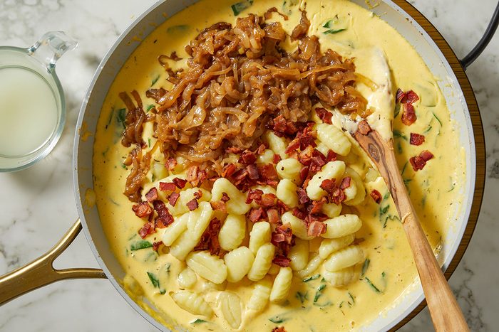 An overhead, horizontal step-by-step image of potato gnocchi tossed with creamy sauce, caramelized onions, spinach, and bacon for Million-Dollar Gnocchi.