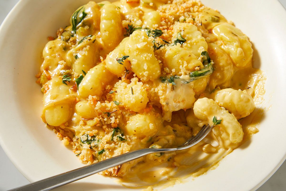An overhead, horizontal close-up image highlighting the creamy texture of Million-Dollar Gnocchi with visible cheese sauce, gnocchi pillows, and breadcrumb topping.
