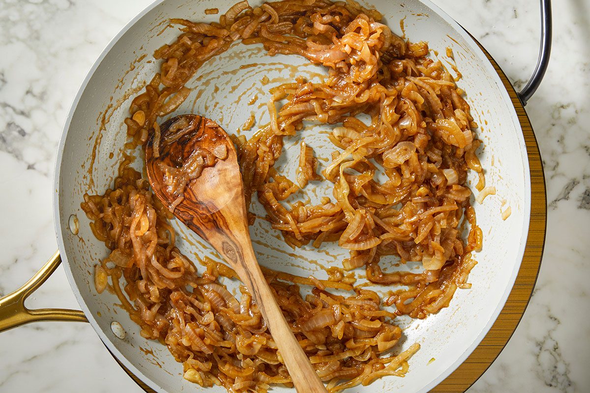 An overhead, horizontal step-by-step image of fully caramelized onions cooked until golden brown in a skillet, ready to be added to Million-Dollar Gnocchi.