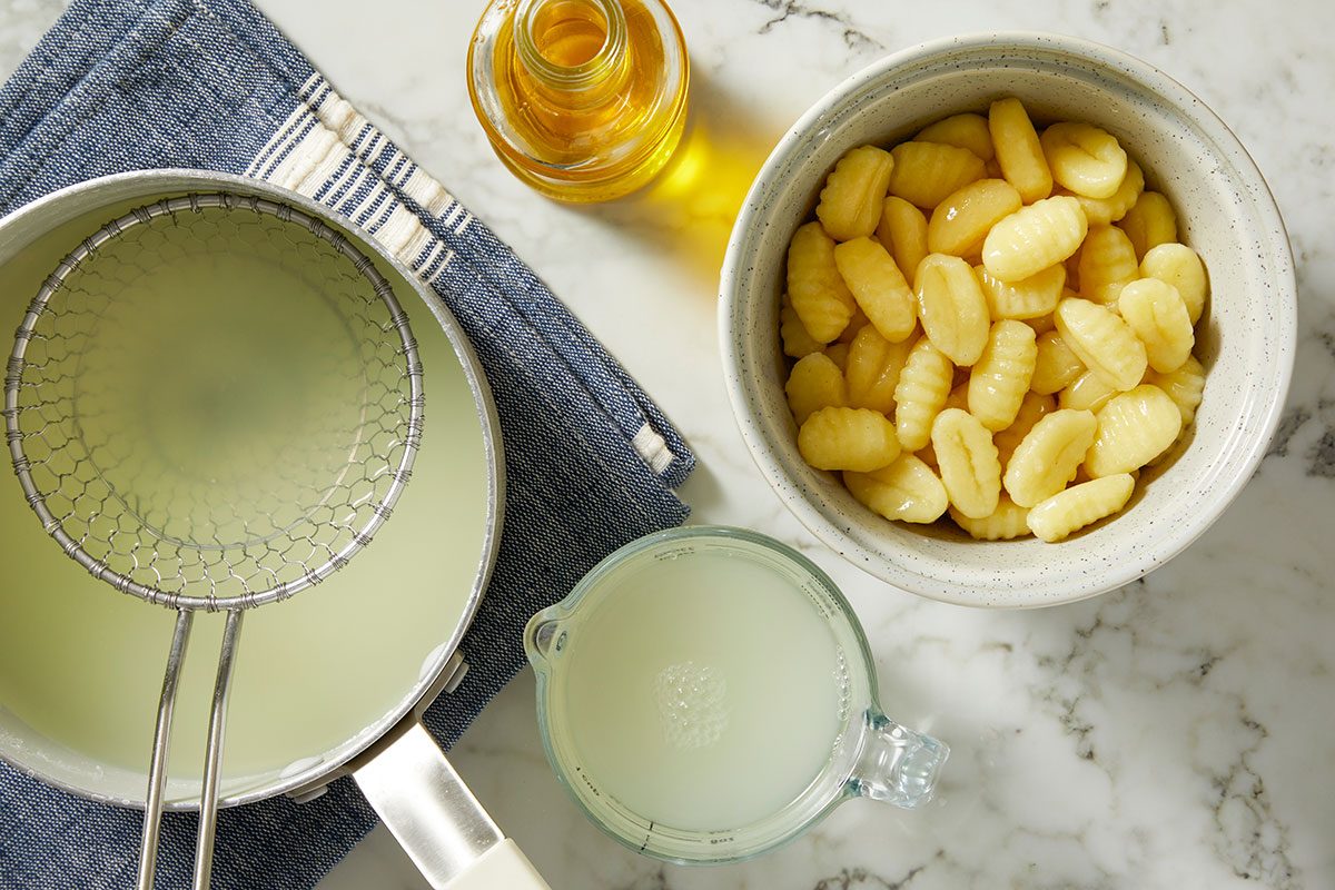 An overhead, horizontal step-by-step image showing potato gnocchi alongside prepared ingredients including broth, cream, and aromatics for Million-Dollar Gnocchi.