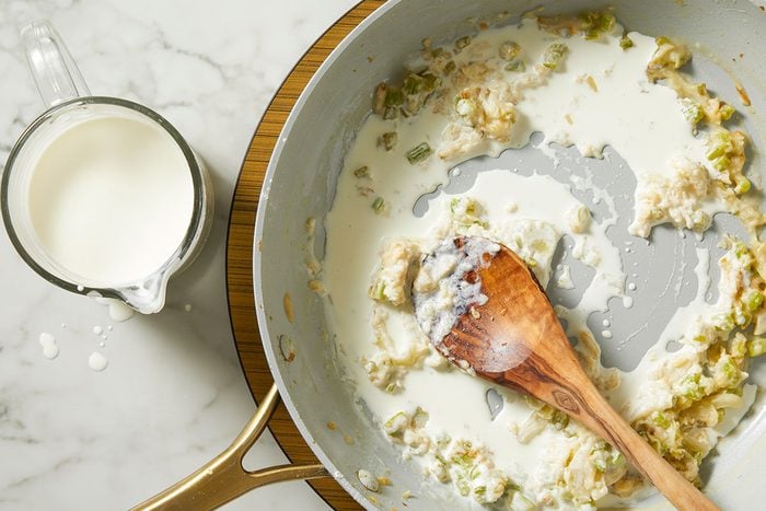 An overhead, horizontal step-by-step image showing flour and white wine stirred into sautéed vegetables to create the creamy sauce base for Million-Dollar Gnocchi.