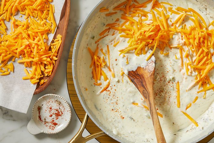 An overhead, horizontal step-by-step image of heavy whipping cream and shredded cheddar cheese being stirred into the sauce for Million-Dollar Gnocchi.