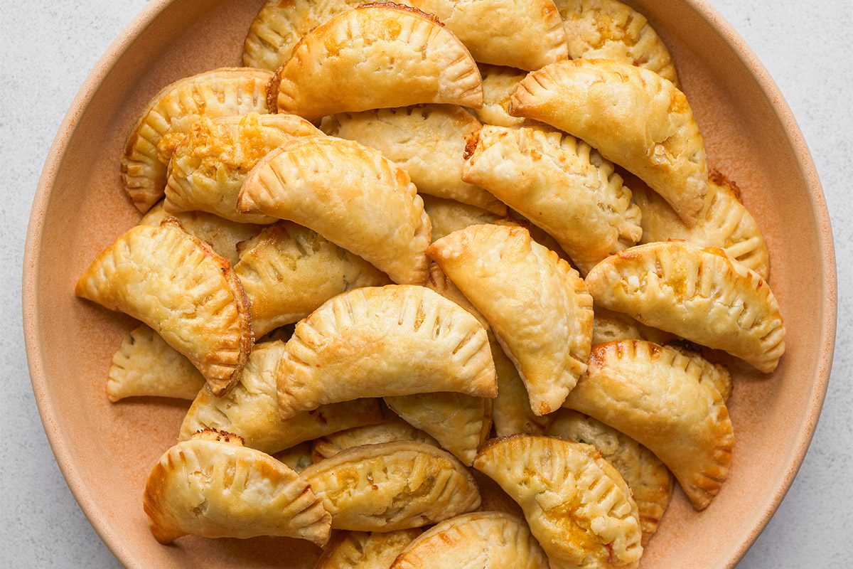 Overhead shot of a round plate filled with golden-brown, half-moon Mini Chicken Empanadas arranged in a circular pattern;