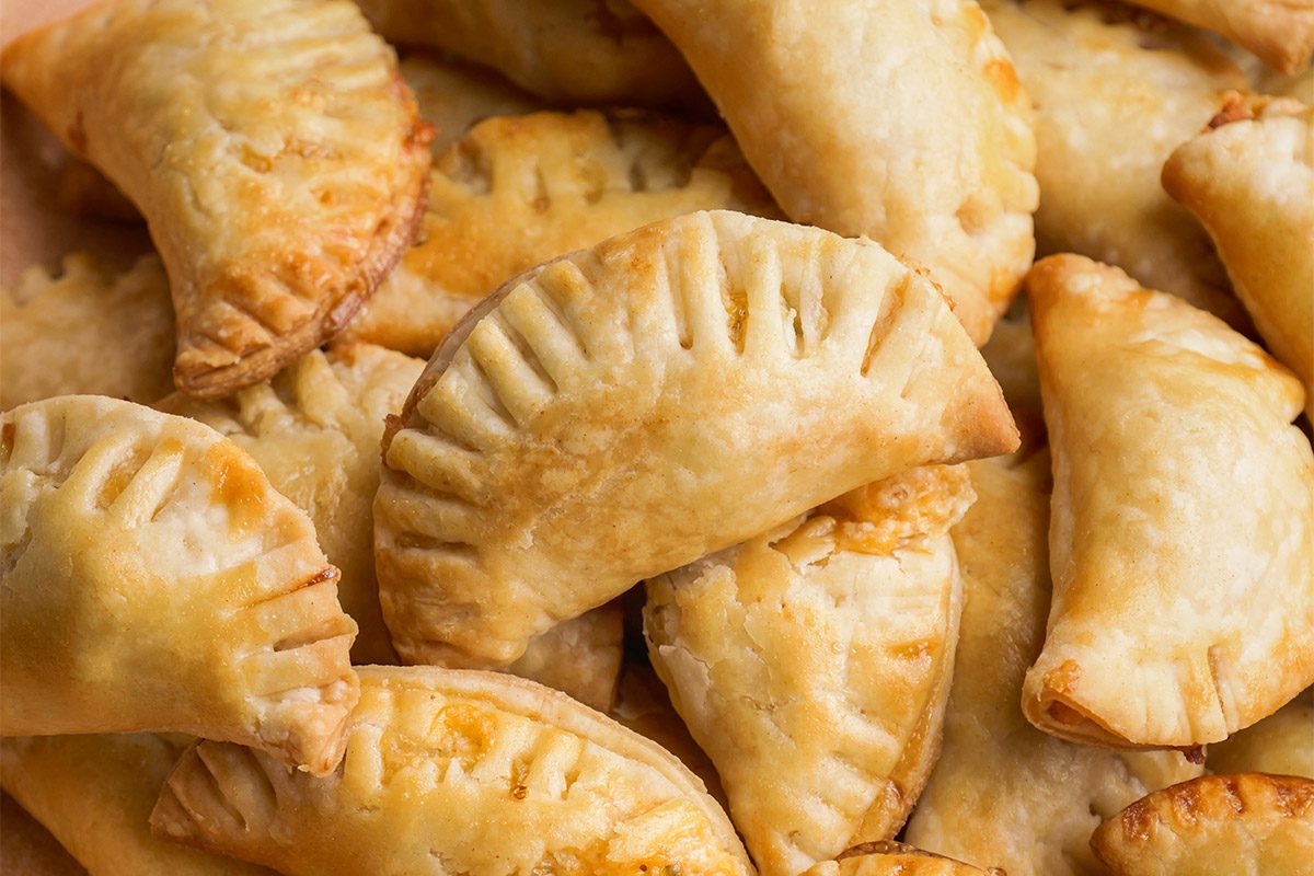 Closeup shot of several golden-brown Mini Chicken Empanadas with crimped edges, piled together to show their flaky, baked pastry crust;