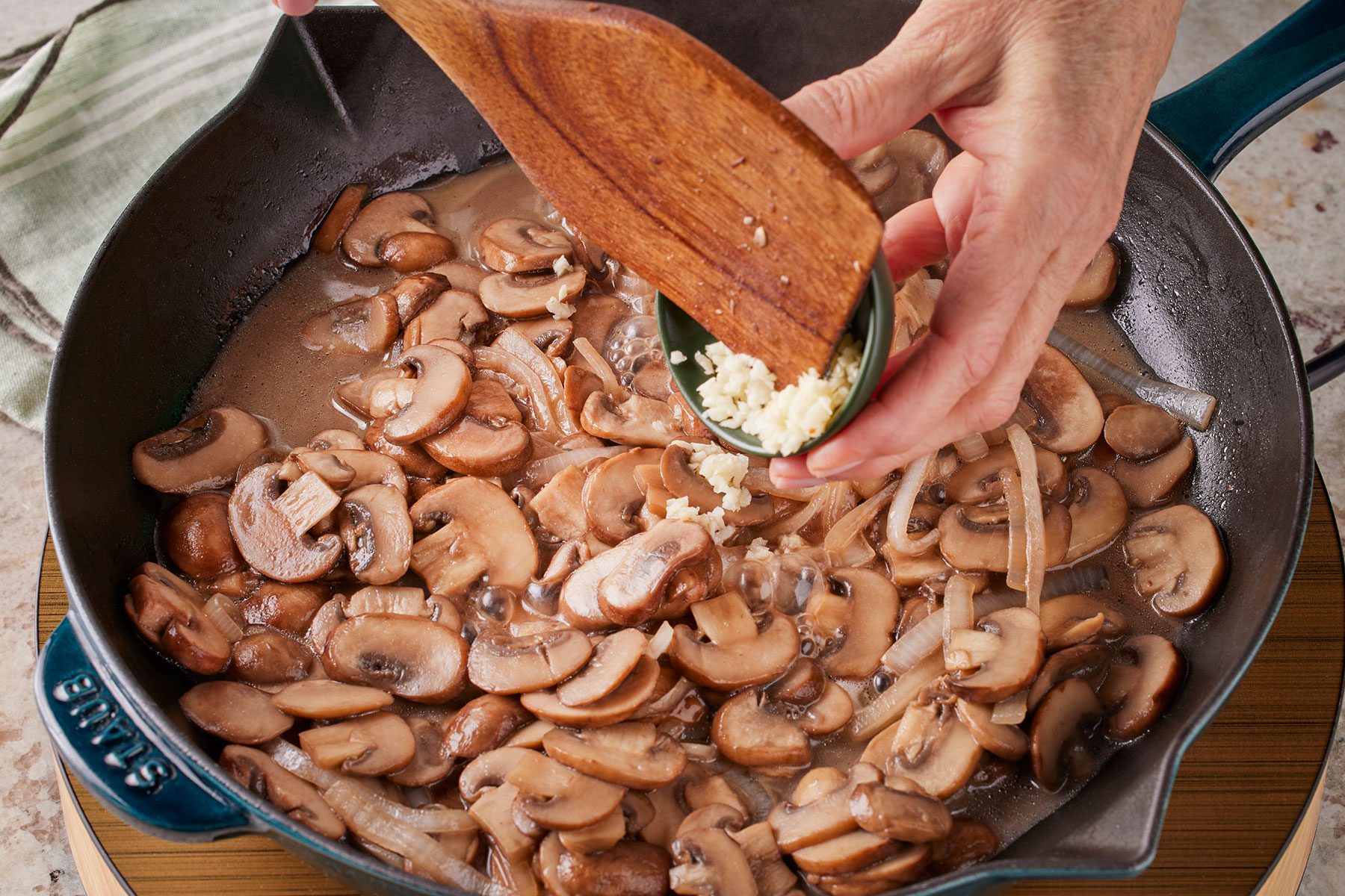 Adding minced garlic to sautéed mushrooms in a large skillet.