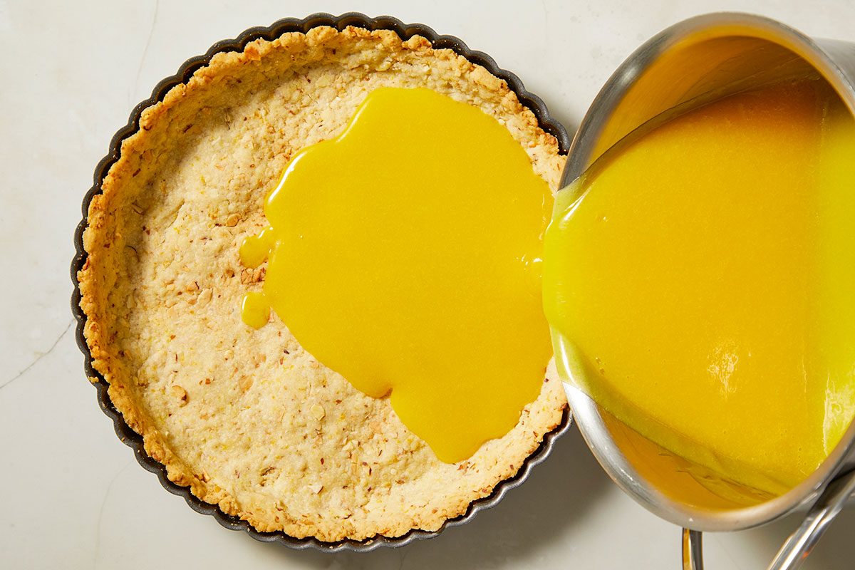Overhead, horizontal step-by-step image showing passion fruit filling being poured into a prepared almond tart crust before baking.
