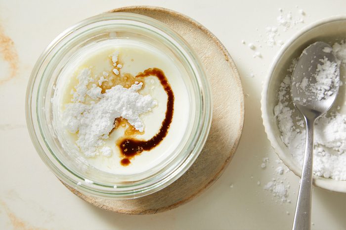 Overhead shot of cream cheese, confectioners’ sugar, and vanilla extract combined in a glass container, beginning the process of making a smooth whipped cream topping for the Red Velvet Espresso Martini.