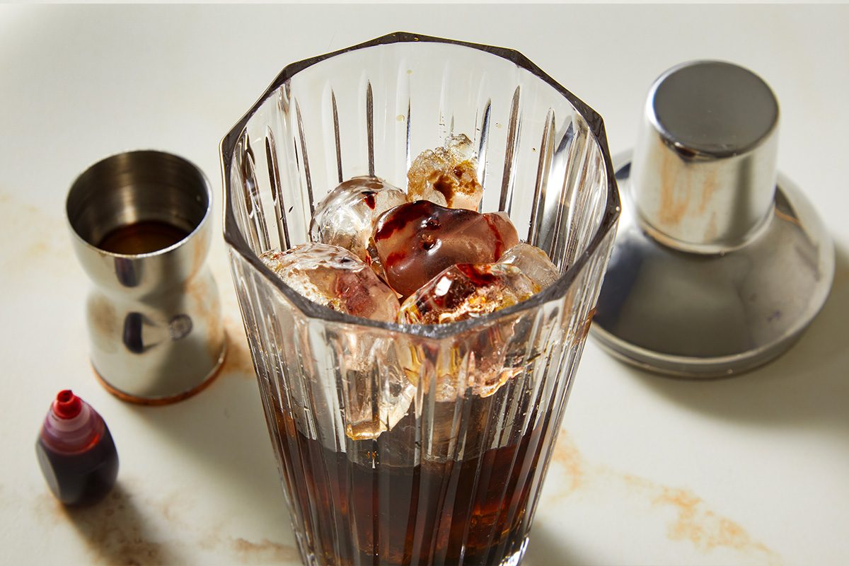 Overhead shot of a blender jar filled with ice, espresso, vodka, coffee liqueur, chocolate liqueur, red velvet cake extract, and red food coloring, capturing the mixing stage of the Red Velvet Espresso Martini.