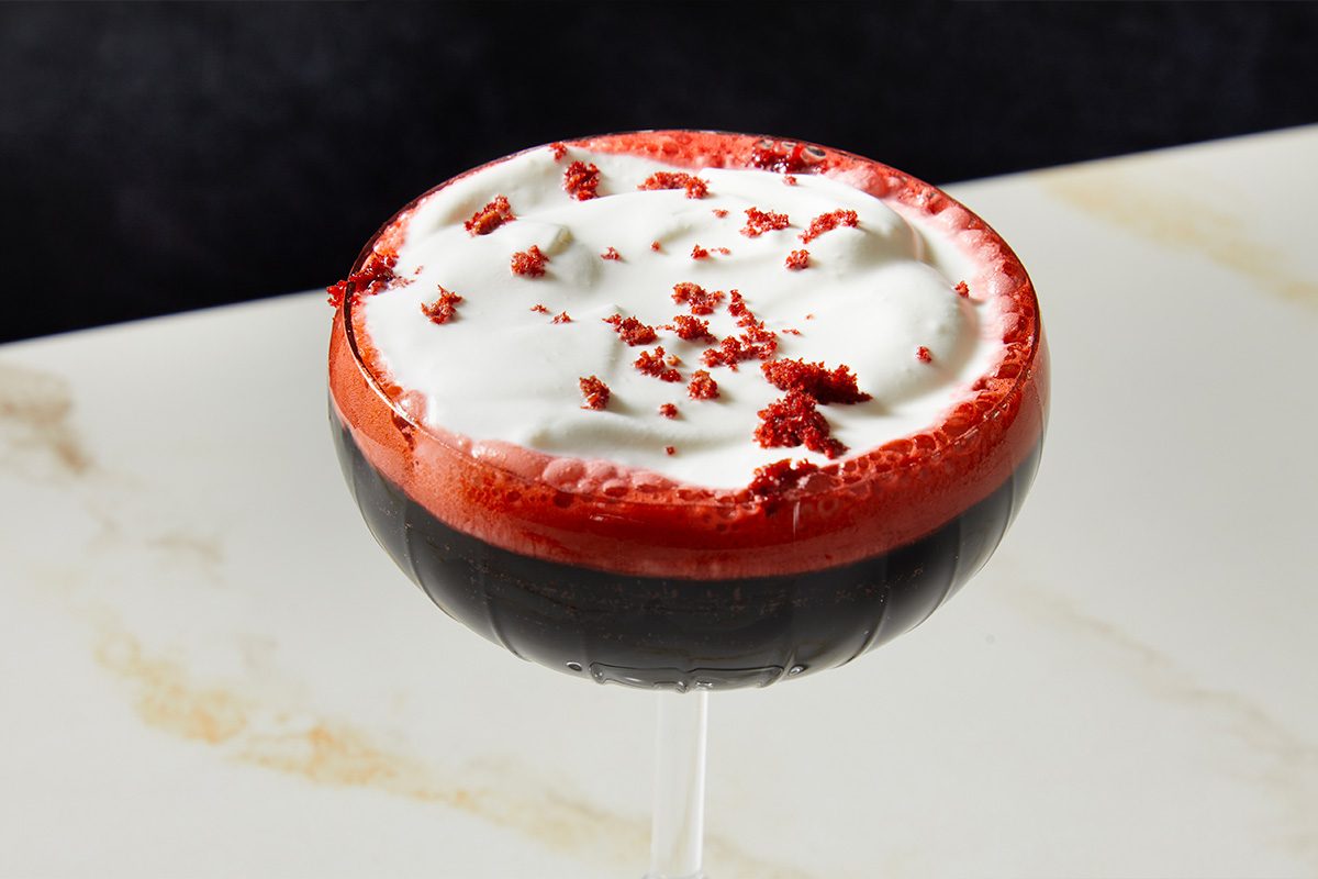 Close-up overhead view of a single Red Velvet Espresso Martini, highlighting the smooth whipped topping and evenly scattered red velvet cake crumbs.