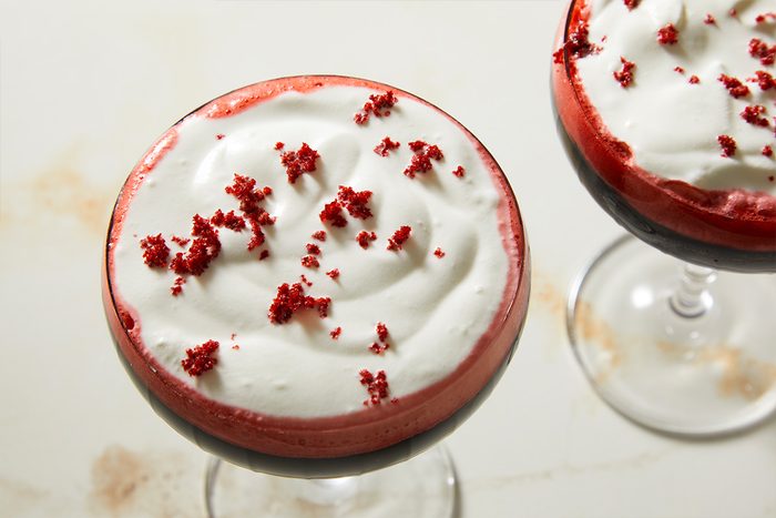 Tight overhead shot of the finished Red Velvet Espresso Martini showing the contrast between the deep red cocktail base, white cream topping, and red velvet cake crumb garnish.